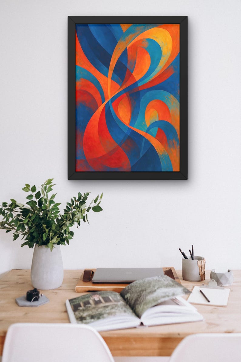 May include: Abstract art print in a black frame. The artwork features flowing, curved shapes in shades of blue, orange, and red. The framed art is displayed above a wooden desk with a vase of greenery, a laptop, and an open book.
