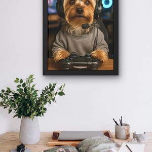 Pu&ograve; includere: Stampa incorniciata di uno Yorkshire Terrier con cuffie e maglione grigio, che tiene in mano un controller di videogiochi nero. Il cane &egrave; il soggetto principale, su uno sfondo sfocato. La stampa &egrave; su una scrivania di legno con una pianta e altri oggetti.