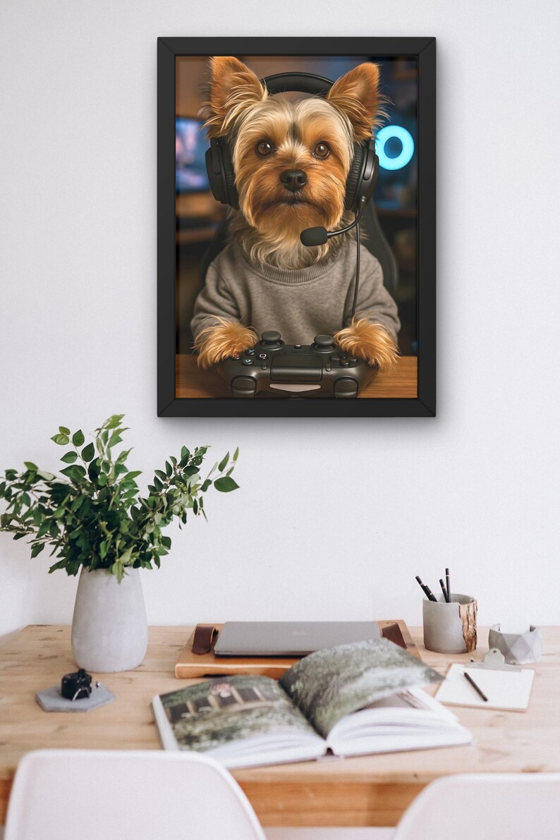 Pu&ograve; includere: Stampa incorniciata di uno Yorkshire Terrier con cuffie e maglione grigio, che tiene in mano un controller di videogiochi nero. Il cane &egrave; il soggetto principale, su uno sfondo sfocato. La stampa &egrave; su una scrivania di legno con una pianta e altri oggetti.