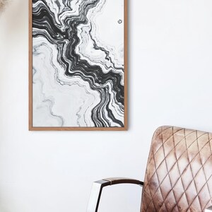 May include: Abstract art print in a wooden frame. The artwork features a flowing, marbled design in shades of black and white. The print is displayed on a white wall, with a brown leather armchair in the foreground.