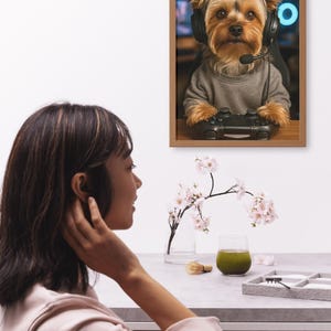 Pu&ograve; includere: Stampa incorniciata con un Yorkshire Terrier con cuffie e un controller di gioco. Il cane indossa un maglione grigio. L'immagine &egrave; ambientata su uno sfondo sfocato con un anello al neon blu.