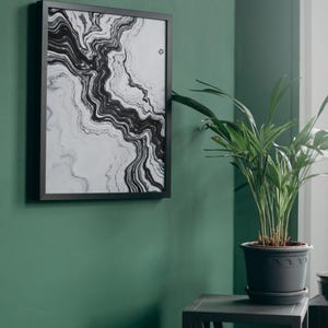 May include: A framed abstract art print with a black and white marble design hangs on a dark green wall. A potted plant sits on a small gray table next to the artwork. The room has a modern, minimalist aesthetic.