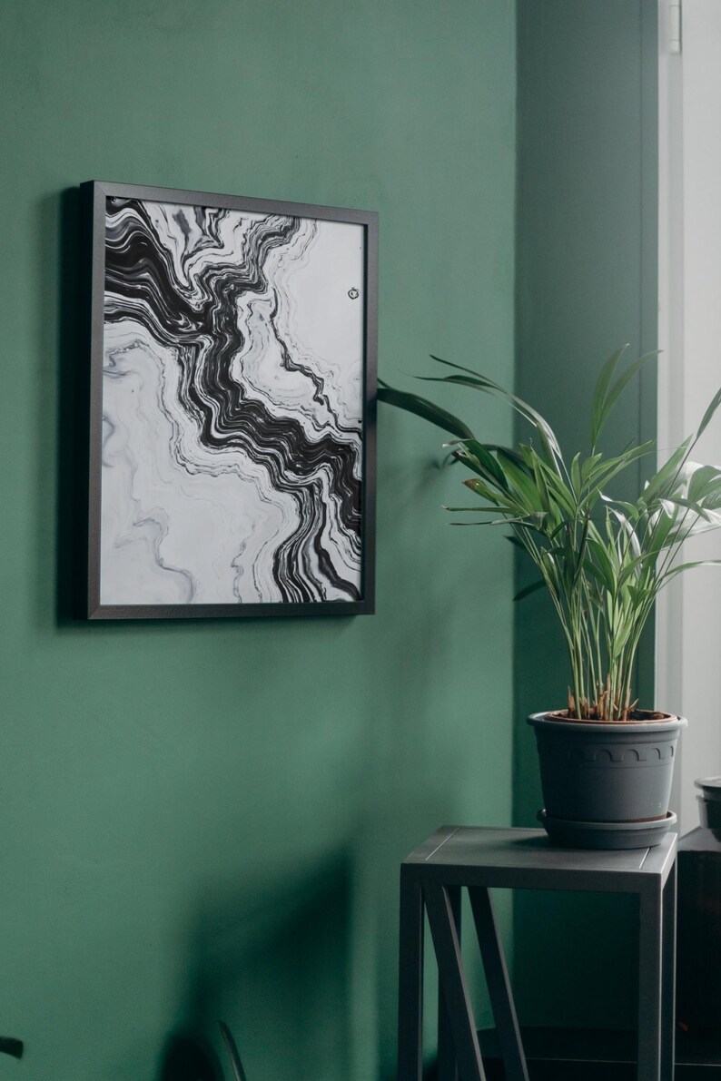 May include: A framed abstract art print with a black and white marble design hangs on a dark green wall. A potted plant sits on a small gray table next to the artwork. The room has a modern, minimalist aesthetic.