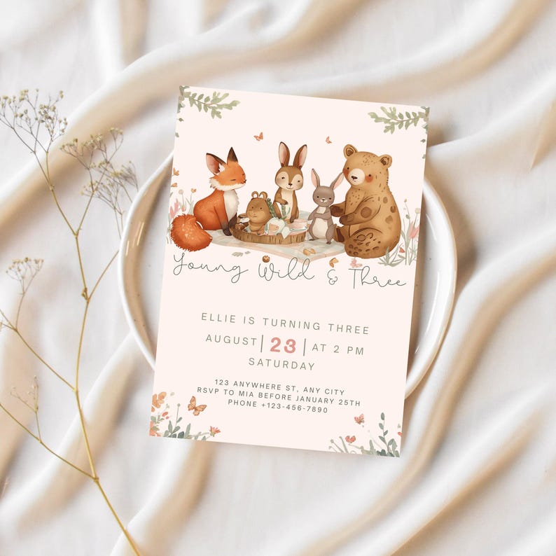 May include: A light pink birthday invitation with watercolor illustrations of woodland animals. The text reads "Young Wild & Three" and includes party details: date, time, and location. Decorative floral and butterfly accents frame the invitation.