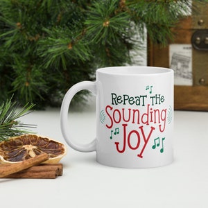 May include: White ceramic mug with a green and red design. The mug says "Repeat the Sounding Joy" with musical notes.