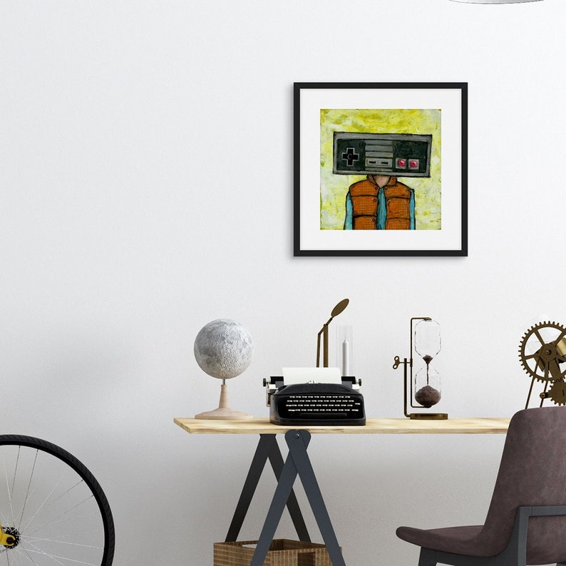 May include: A framed illustration of a person with a retro video game controller for a head. The person is wearing a blue shirt and an orange vest. The background is yellow.