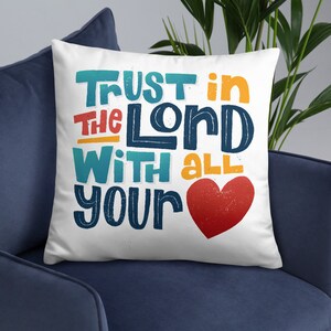 Op de afbeelding: Een wit kussen met de tekst "Trust in the Lord with all your" in kleurrijke letters en een rood hart.