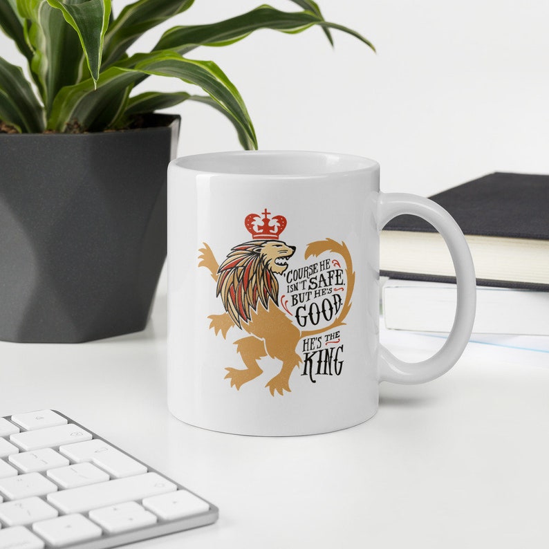May include: White ceramic mug with a lion graphic and the text "Course he isn't safe, but he's good. He's the King."