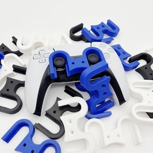 Könnte beinhalten: Ein weiß-schwarzer Gamecontroller mit blauen und schwarzen Zubehörteilen. Das Zubehör hat die Form eines "U" und ist um den Controller herum verstreut. Der Controller hat Tasten und zwei Joysticks.