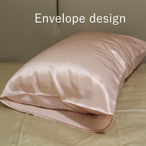 May include: A blush-colored satin pillowcase with an envelope design. The pillowcase is rectangular and has a smooth, shiny texture. The words "Envelope design" are printed in white on the top left.