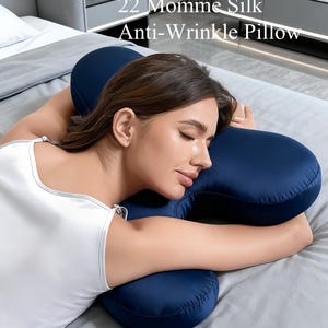 May include: A navy blue silk anti-wrinkle pillow with the text "22 Momme Silk Anti-Wrinkle Pillow." The pillow has a unique shape designed for comfort and support. The image shows the pillow on a bed.