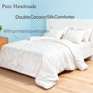 May include: A white bed set with a printed duvet cover, pillows, and a comforter. The text in the image reads "Pure Handmade Double Cocoon Silk Comforter With printed duvet cover."