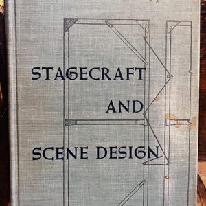 May include: A vintage book titled "Stagecraft and Scene Design" by Philippi. The cover is a muted green with black text and architectural diagrams. The book's cover has a linen texture.