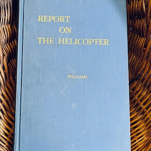 May include: A vintage book titled "Report on the Helicopter" by Williams. The book has a light blue cover with gold lettering. The book is resting on a woven basket.