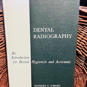 May include: A hardcover book titled "Dental Radiography" with a white spine and a dark green cover. The text includes "An Introduction for Dental Hygienists and Assistants" and the author's name, Richard C. O'Brien.