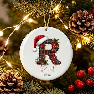Könnte beinhalten: Ein runder, weißer Keramik-Weihnachtsbaumschmuck mit einem großen Buchstaben R im rot-grünen Schottenkaro-Muster, verziert mit bunten Lichterketten und einer Weihnachtsmütze. Darunter steht der Name Rachel in roter Schrift und das Jahr 2026 in Grün.