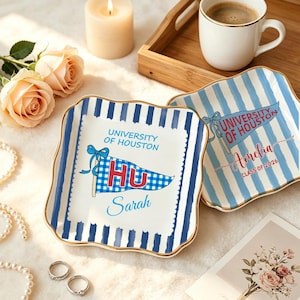 May include: Two square ceramic plates with blue and white stripes and gold trim. One plate features a pennant with "University of Houston" and "HU" text, and the name "Sarah". The other plate has "Amelia" and "Class of 2026".