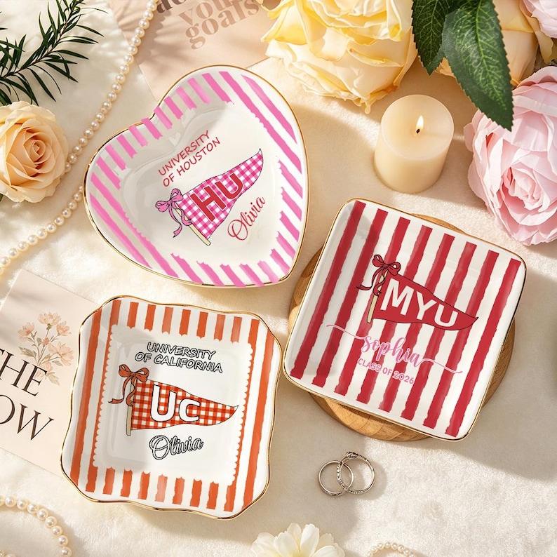 May include: Three decorative ceramic dishes with gold trim. One is heart-shaped with pink stripes and "University of Houston" text. Another is square with red stripes and "MYU" text. The third is square with orange stripes and "University of California" text.