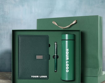 May include: A dark green gift set featuring a notebook, pen, and insulated tumbler. The notebook has a silver clasp and the text "YOUR LOGO". The tumbler has the text "YOUR LOGO" in white. The set is presented in a green box with a matching gift bag.
