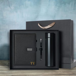 May include: A black gift set containing a notebook with gold lettering "TY", a pen, and a black insulated water bottle. The items are presented in a black box with a matching gift bag.