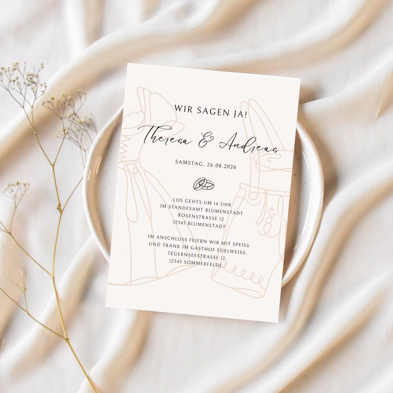 May include: A cream-colored wedding invitation with the text "WIR SAGEN JA!" and the names "Theresa & Andreas." The invitation includes the date, time, and location of the ceremony and reception. The design features line art of a bride and groom.