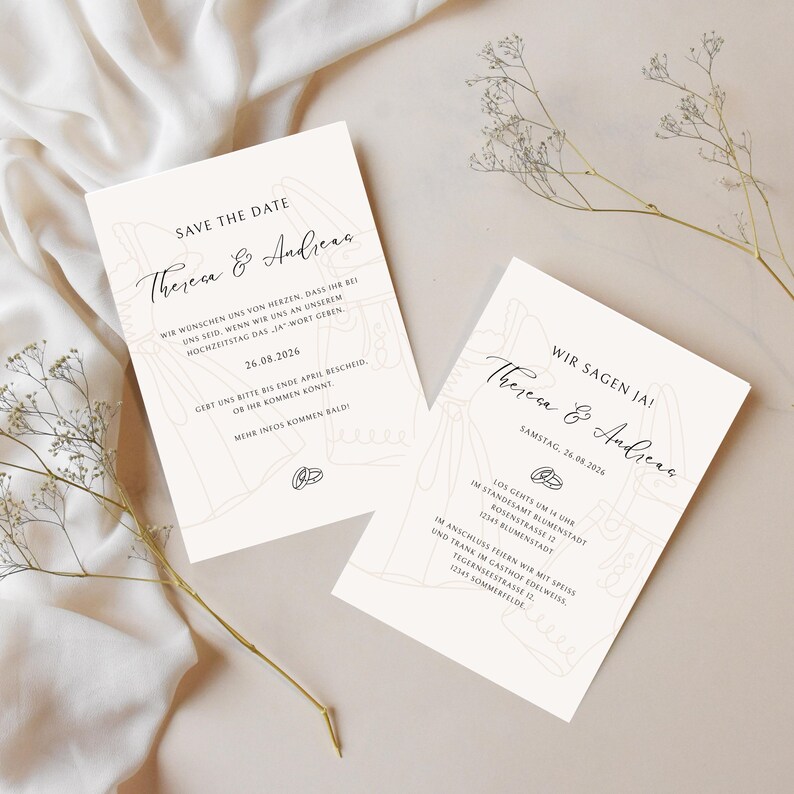 May include: Two cream-colored wedding invitation cards with elegant script text. The cards feature the names "Theresa & Andreas" and the date "26.08.2026". Delicate line drawings of wedding attire and rings adorn the design.