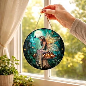 May include: Round stained glass panel featuring a fairy sitting on a mushroom in a forest scene. The fairy has large, colorful wings and is surrounded by butterflies. The panel is held by a gold chain and is displayed in front of a window.