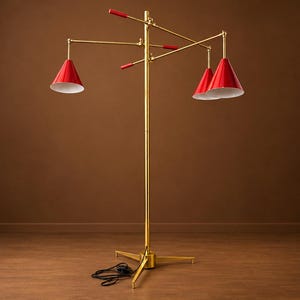 May include: A floor lamp with a central brass pole and a tripod base. It features three adjustable arms with red conical shades and white interiors. The arms have red handles for positioning, and a black power cord extends from the base.