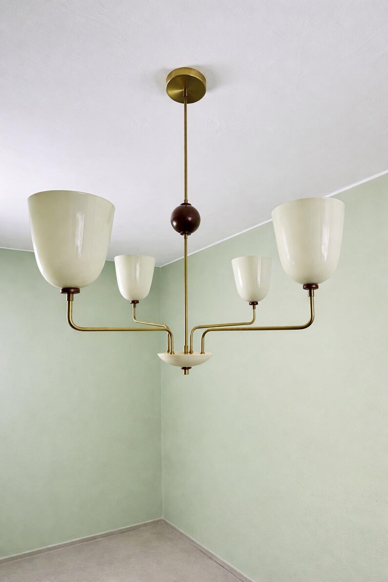 May include: A mid-century modern chandelier with four off-white, tulip-shaped shades. The fixture has brass arms and a dark brown sphere. The ceiling mount is brass, and the fixture hangs in a room with pale green walls.