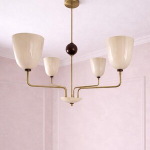 May include: A mid-century modern chandelier with five off-white, tulip-shaped shades. The fixture has brass-colored arms and a central stem with a dark brown sphere. The chandelier is suspended from a brass-colored ceiling mount.