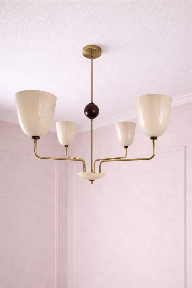 May include: A mid-century modern chandelier with five off-white, tulip-shaped shades. The fixture has brass-colored arms and a central stem with a dark brown sphere. The chandelier is suspended from a brass-colored ceiling mount.