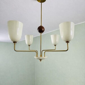 May include: A mid-century modern chandelier with five off-white, tulip-shaped glass shades. The fixture has brass arms and a dark wood sphere detail. The ceiling mount is brass.