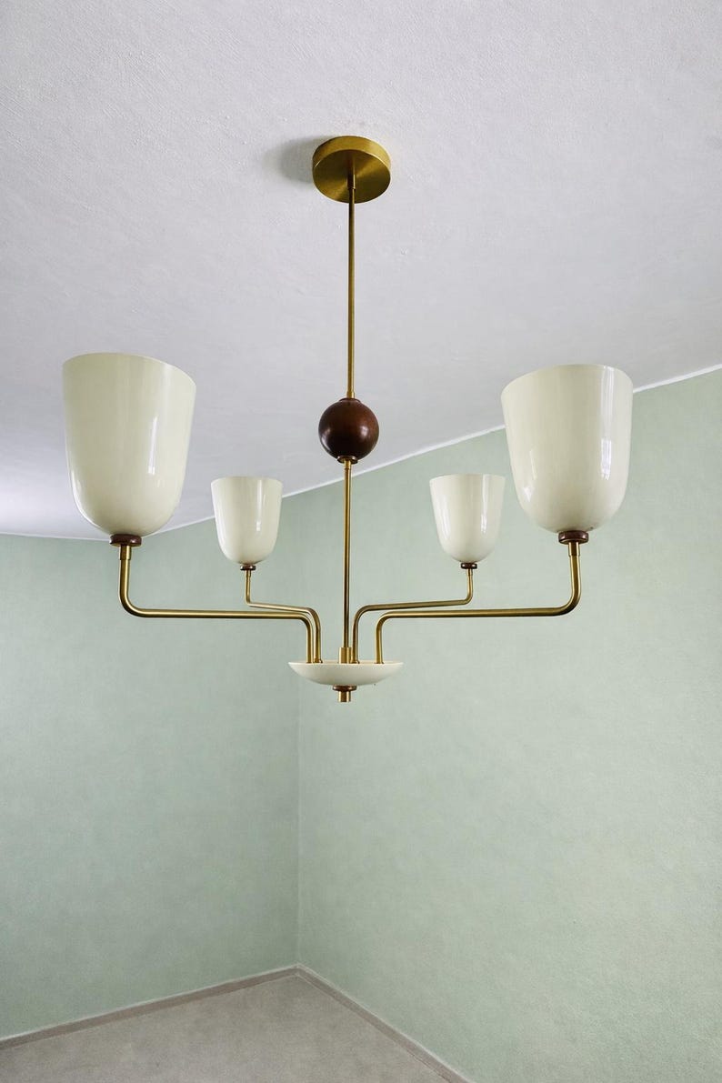 May include: A mid-century modern chandelier with five off-white, tulip-shaped glass shades. The fixture has brass arms and a dark wood sphere detail. The ceiling mount is brass.