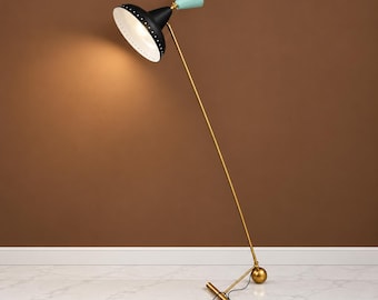 May include: A floor lamp featuring a long, thin gold-toned metal stand and a base with a spherical accent. The lamp head is a black, wide-brimmed shade with a white interior and a small, light blue conical top piece, angled to provide illumination.