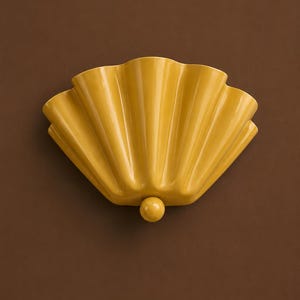 Peut inclure: Une applique murale en céramique jaune moutarde en forme d'éventail ou de coquillage avec des cannelures verticales. Le luminaire présente une finition lisse et brillante ainsi qu'un petit bouton décoratif sphérique au centre de la base.