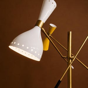 May include: A floor lamp featuring a central brass pole with multiple adjustable arms. The lamp has two white conical shades with perforated edges and one smaller yellow conical shade, all accented with brass hardware and black handle grips.