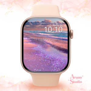 Könnte beinhalten: Eine roségoldene Smartwatch mit einem glatten Silikonarmband. Das digitale Display zeigt die Uhrzeit 10:10 und das Datum SUN 10 über einem lebendigen Bild eines Strandes bei Sonnenuntergang mit violettem und rosa glitzerndem Sand.