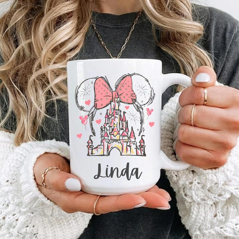 May include: White ceramic mug featuring a pink bow, Mickey Mouse ears, and a castle design. The mug has the name "Linda" printed in black script. Pink hearts and fireworks complete the design. A perfect gift for Disney fans.