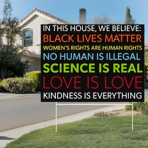 May include: A black yard sign with white lettering that reads "IN THIS HOUSE, WE BELIEVE: BLACK LIVES MATTER WOMEN'S RIGHTS ARE HUMAN RIGHTS NO HUMAN IS ILLEGAL SCIENCE IS REAL LOVE IS LOVE KINDNESS IS EVERYTHING."