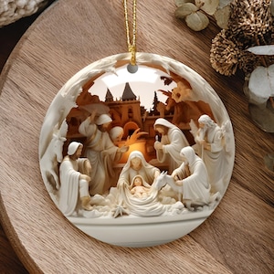 May include: A round, off-white Christmas ornament with a detailed nativity scene. The ornament features figures in flowing robes surrounding a baby in a manger, with a building in the background. A gold string is attached for hanging.