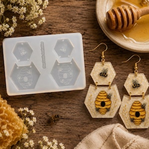 May include: Honeycomb-shaped earrings with gold hooks, featuring bee and beehive designs. A silicone mold with bee and beehive shapes is also present. The image includes a honeycomb, honey, and a wooden honey dipper, all on a wooden surface.