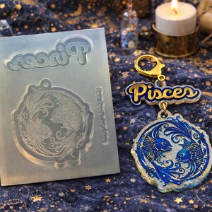 May include: A clear silicone mold and a blue and gold Pisces keychain. The mold has the word "Pisces" and a fish design. The keychain features the word "Pisces" and a circular pendant with two fish.