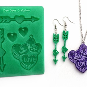 May include: A green silicone mold with arrow and heart shapes, and the text "Dee Dee's Craftables".  Also, green glitter arrow earrings and a purple heart pendant necklace with the words "Be Mine" and "Love".