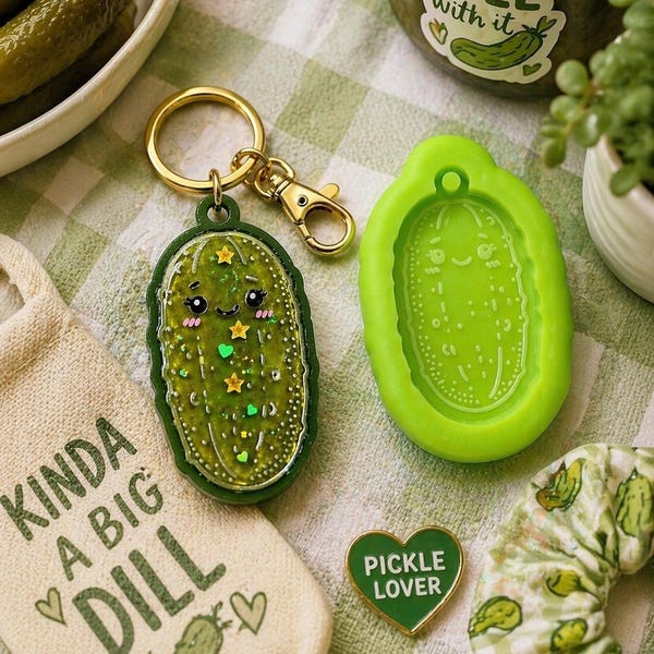 Peut inclure: Plusieurs articles sur le thème du cornichon sont présentés : un porte-clés vert en forme de cornichon souriant, un moule en silicone vert, un sac en toile avec le texte "Kinda a Big Dill", une épingle verte en forme de cœur avec "Pickle Lover" et un chouchou vert et blanc.