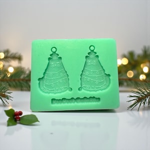 Könnte beinhalten: Eine hellgrüne Silikonform mit zwei katzenförmigen Weihnachtsbaumdesigns. Jede Katze ist mit Lichtern und einem Stern verziert. Der Text "Dee Dee's Craftables" ist am unteren Rand der Form aufgedruckt.