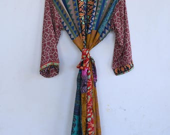 May include: A long-sleeved robe featuring a patchwork design with various colorful patterns including floral, geometric, and chevron prints in shades of red, blue, yellow, and teal. The garment has a wide collar and a matching fabric tie at the waist.