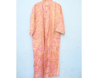 Op de afbeelding: Een lange, openstaande kimono in tinten perzik, roze en paars, met een bloemenpatroon. De kimono hangt aan een houten hanger tegen een lichtblauwe muur. De kimono heeft lange mouwen en twee zakken.