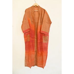 May include: A long, open-front robe in shades of orange and brown, hanging on a wooden hanger. The robe features intricate red embroidered patterns on the front and sleeves, with pockets. The fabric appears lightweight and flowing.