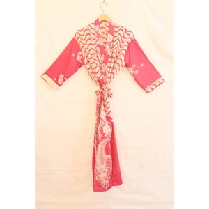 May include: A vibrant pink robe with a cream and pink wavy pattern on the front and sleeves. The robe features a floral design and is tied at the waist. The sleeves and edges are trimmed with a cream border.