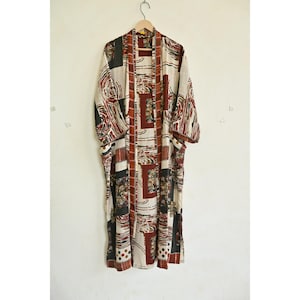 May include: A long, patterned kimono robe in cream, red, black, and brown. The robe is hanging on a wooden hanger against a plain white wall. The design features geometric shapes and floral patterns.